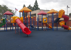 Red and yellow playground equipment with slides and blue turf lining the ground.