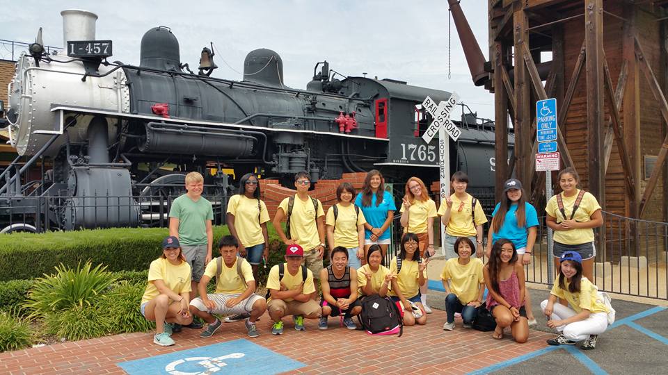Group of exchange students in front of old train at Lomita Railroad Museum