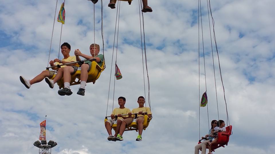 Multiple exchange students in yellow shirts on swings at fair