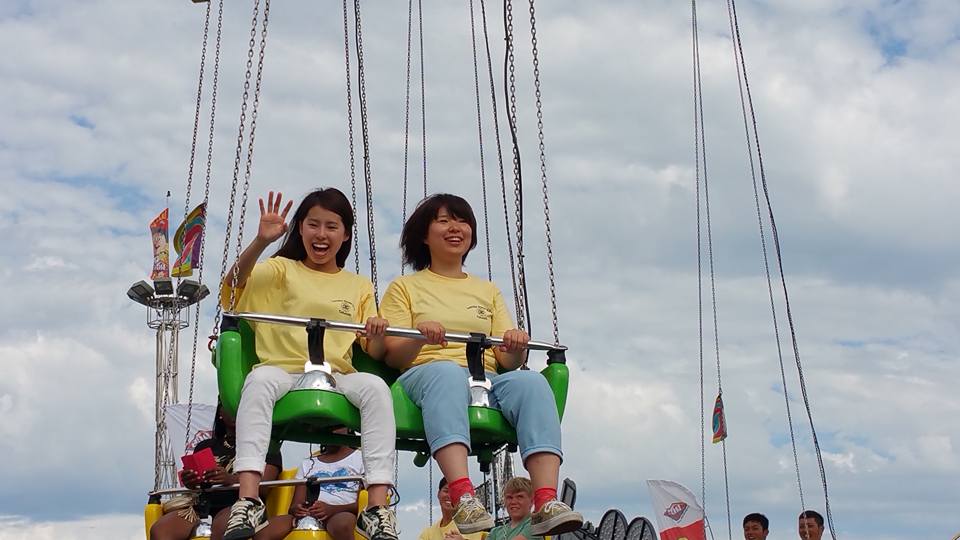 Two exchange students in yellow shirts on swings at fair